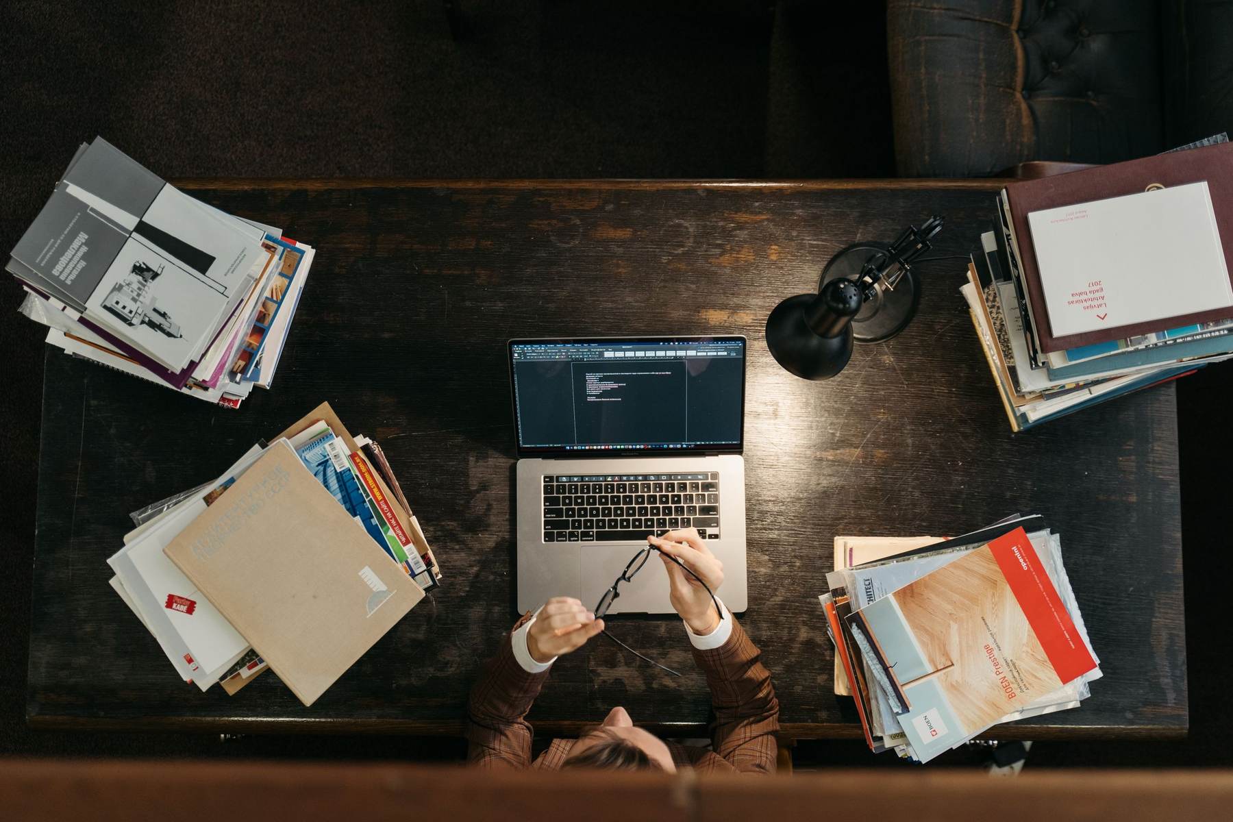 A desk seen from above with a laptop, notebooks and papers
