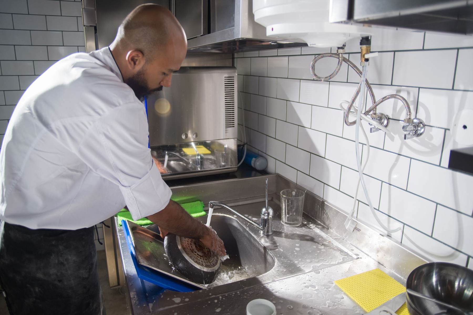 Kitchen worker washing equipment at a sink