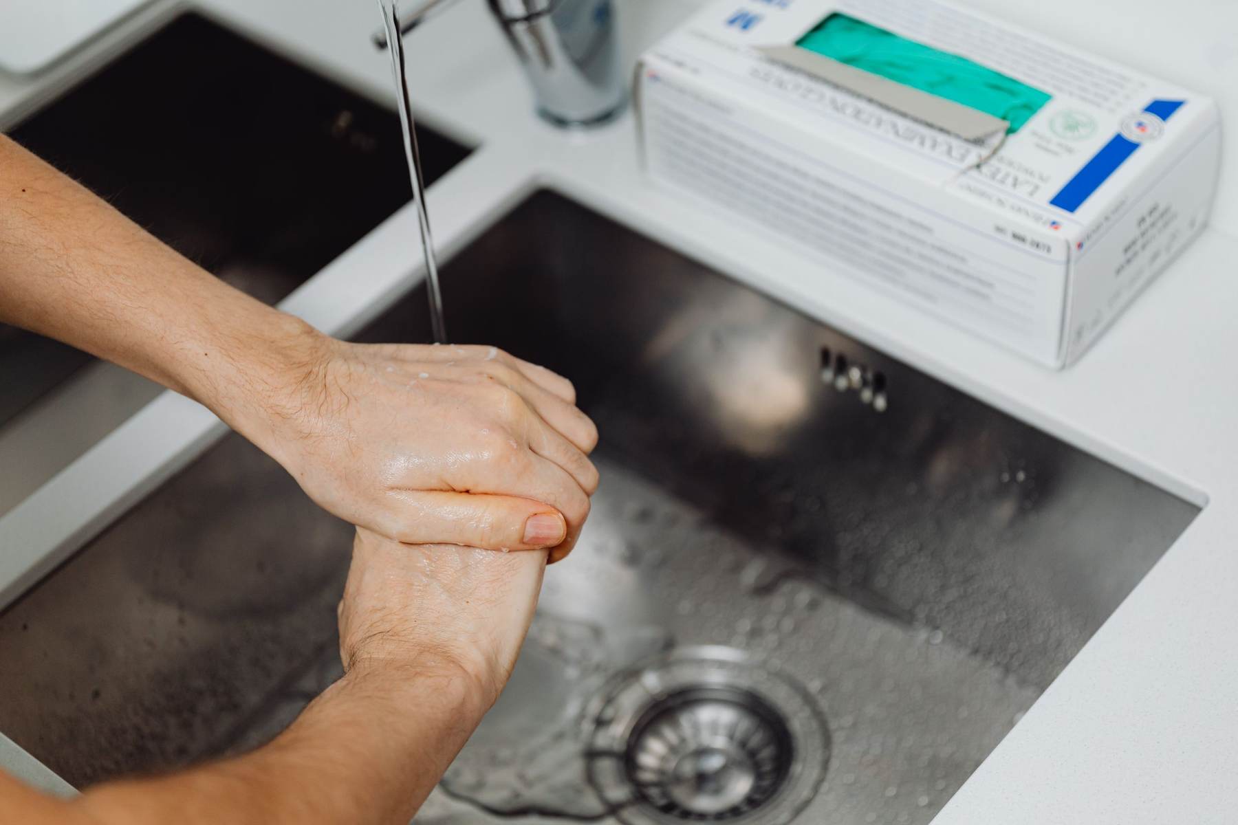 Hands being washed under a tap in a kitchen sink