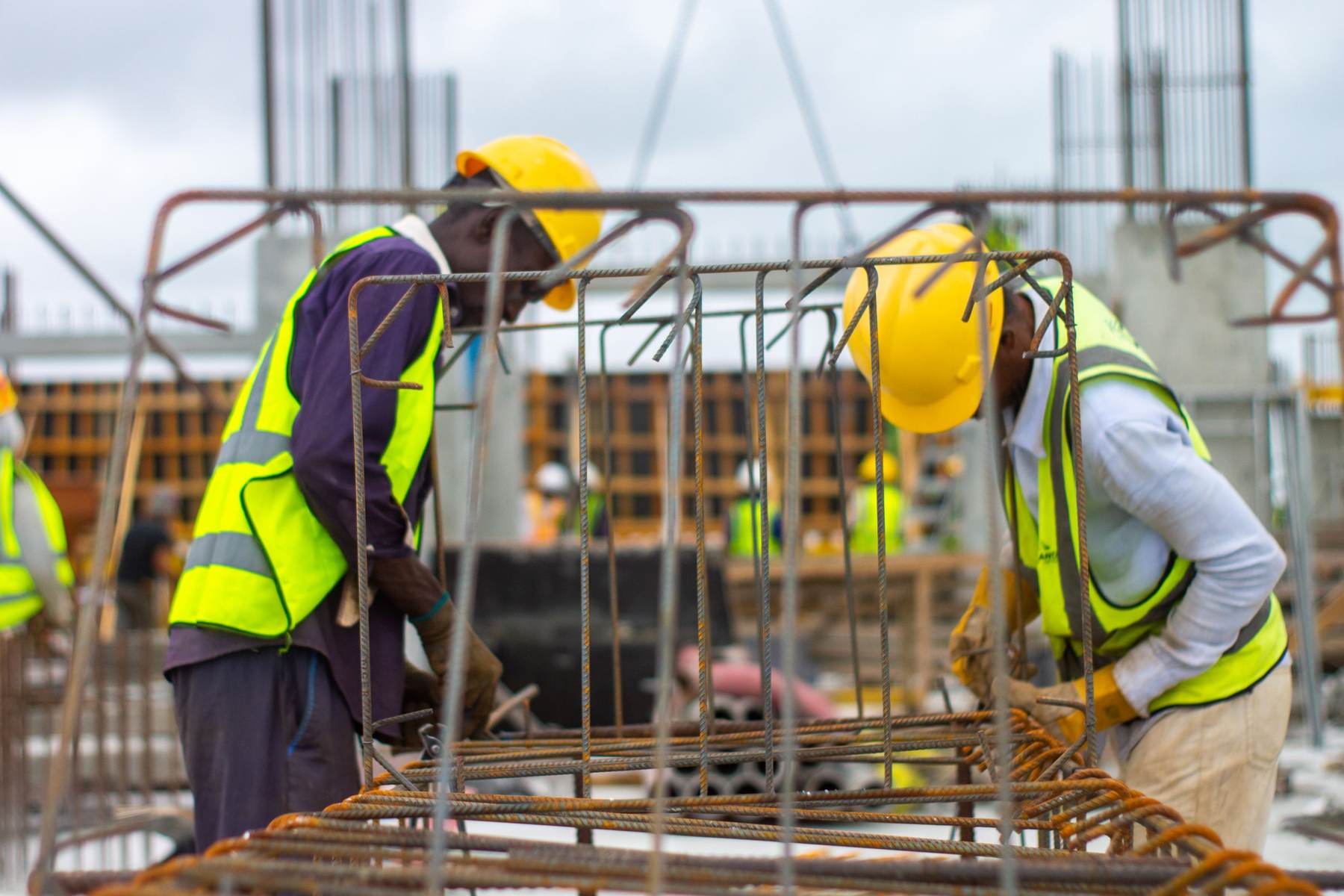 Two site workers in hard hats and high-visibility vests working on reinforcement bars